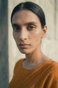 Woman wearing an orange saree against a neutral background