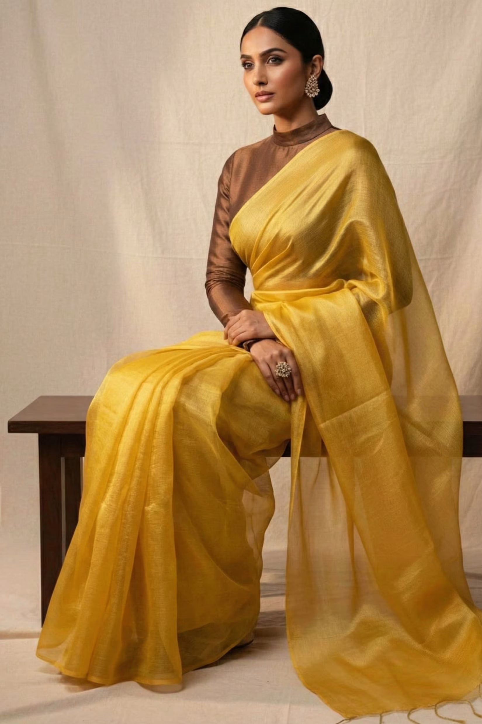 Woman wearing a yellow saree sitting on a bench against a plain background