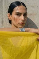 Woman holding a yellow mul cotton saree against a stone wall