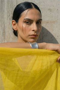 Woman holding a yellow mul cotton saree against a stone wall