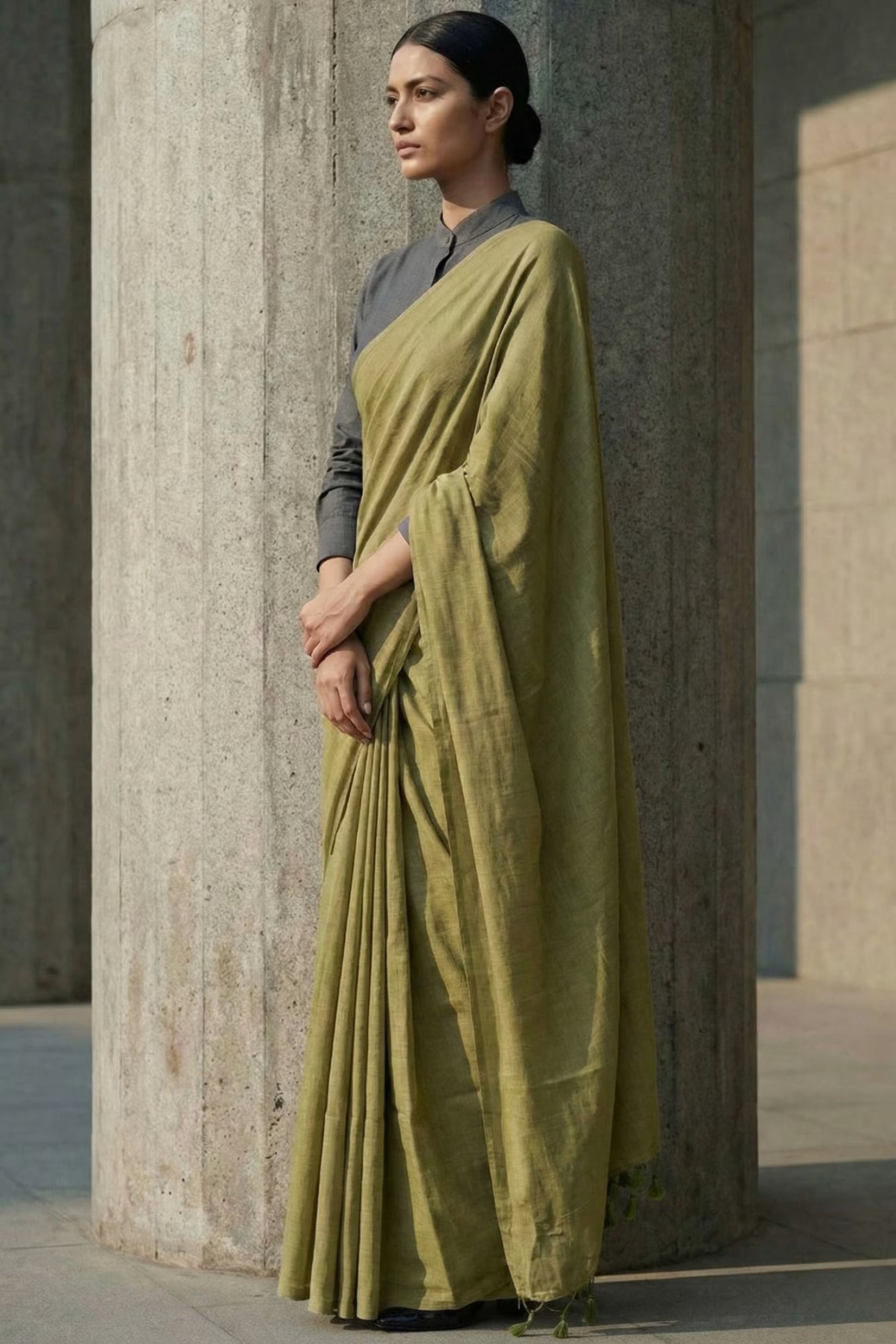 Woman wearing a green saree standing against a stone wall.