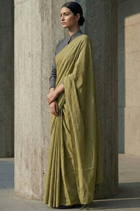 Woman wearing a green saree standing against a stone wall.
