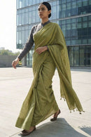 Woman in a green saree walking outdoors with modern building in the background