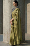 Woman wearing a green saree standing against a stone wall.